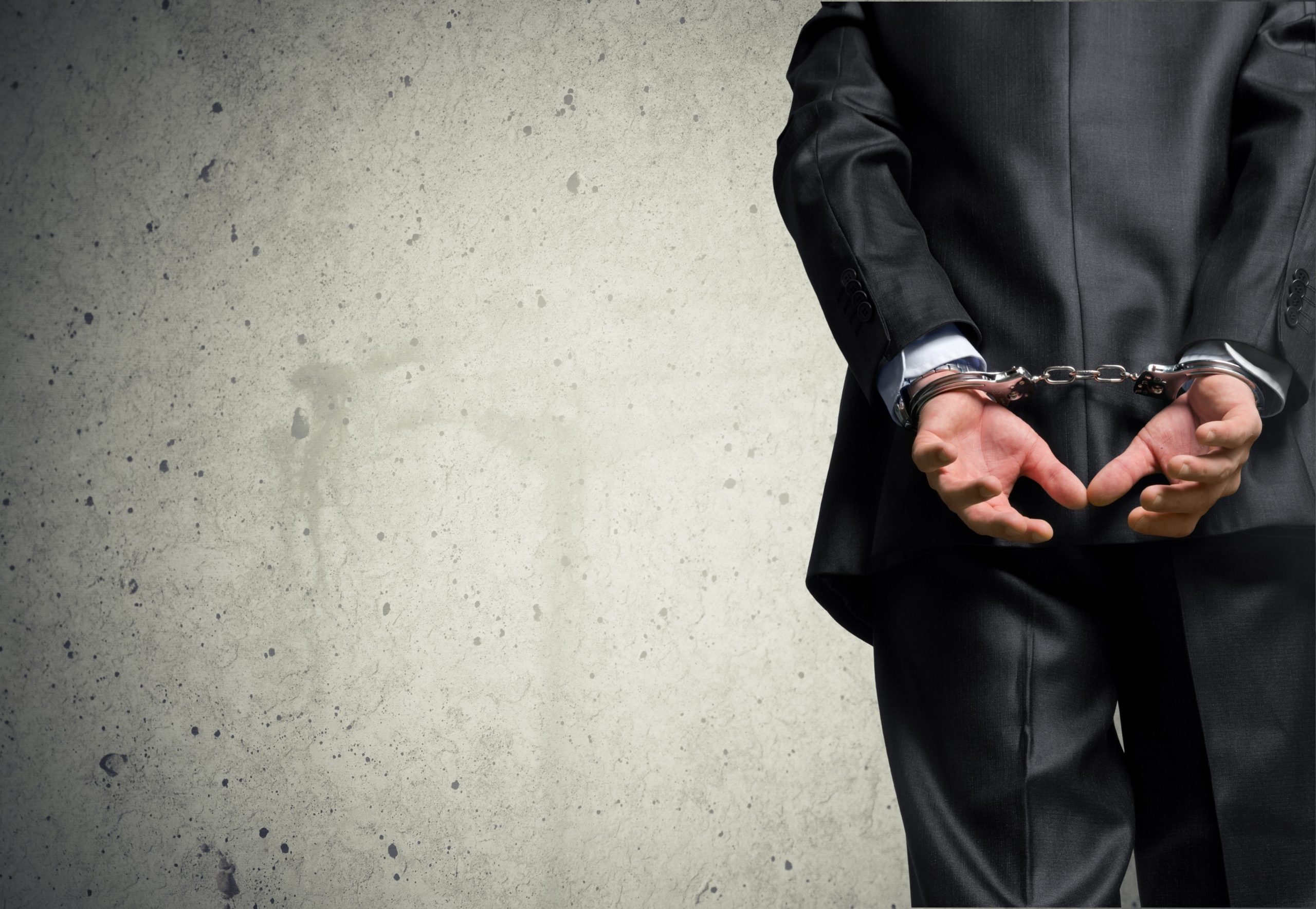 A photo of a man in a suit with handcuffs to represent white-collar crime